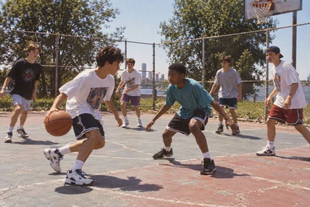 A pickup basketball game spills across a sun-faded outdoor court on a long summer afternoon.