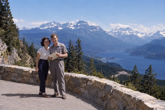 Two young holidaymakers pause at a mountain lookout, windswept and pleased with themselves.