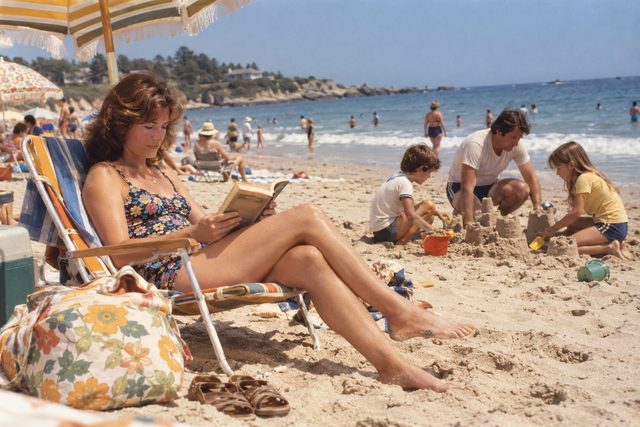 A paperback in the shade while a sandcastle grows nearby.