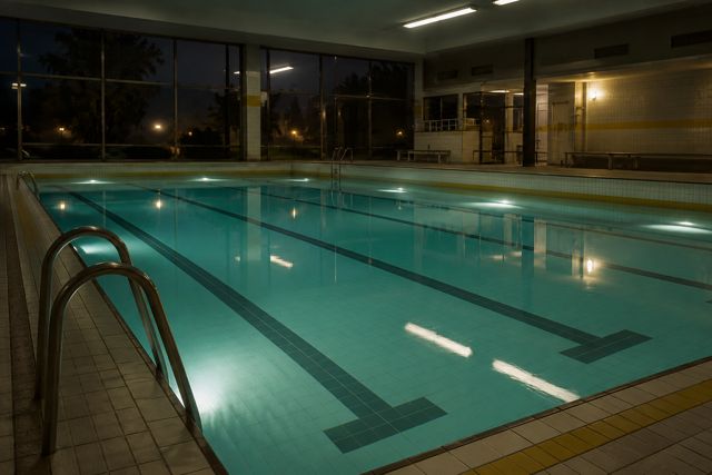 Blue water, vacant lanes, and fluorescent light in an indoor pool that feels suspended in time.