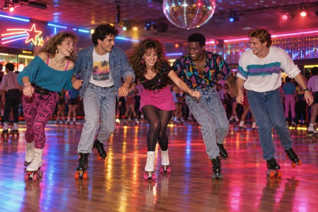 Coloured lights sweep over a lively roller rink while friends try to keep their balance.