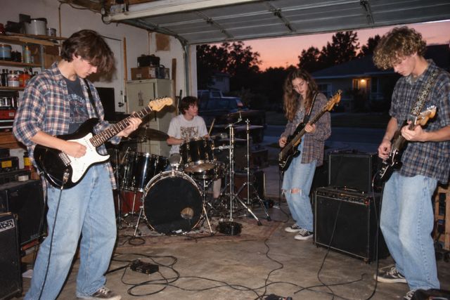 A cluttered garage becomes a rehearsal space, with old amplifiers, tangled cables, and friends making a lot of noise.